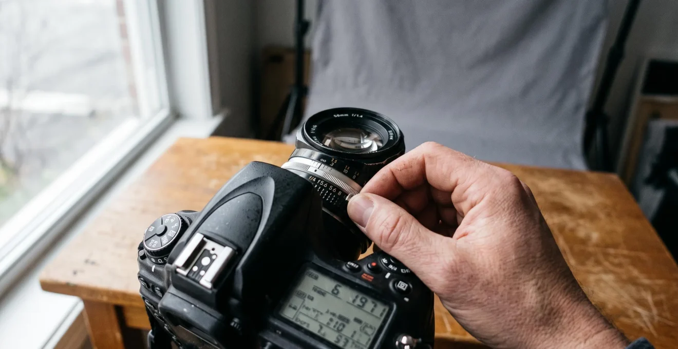 Gros plan sur les mains d'un photographe réglant la bague d'ouverture d'un objectif monté sur un boîtier.